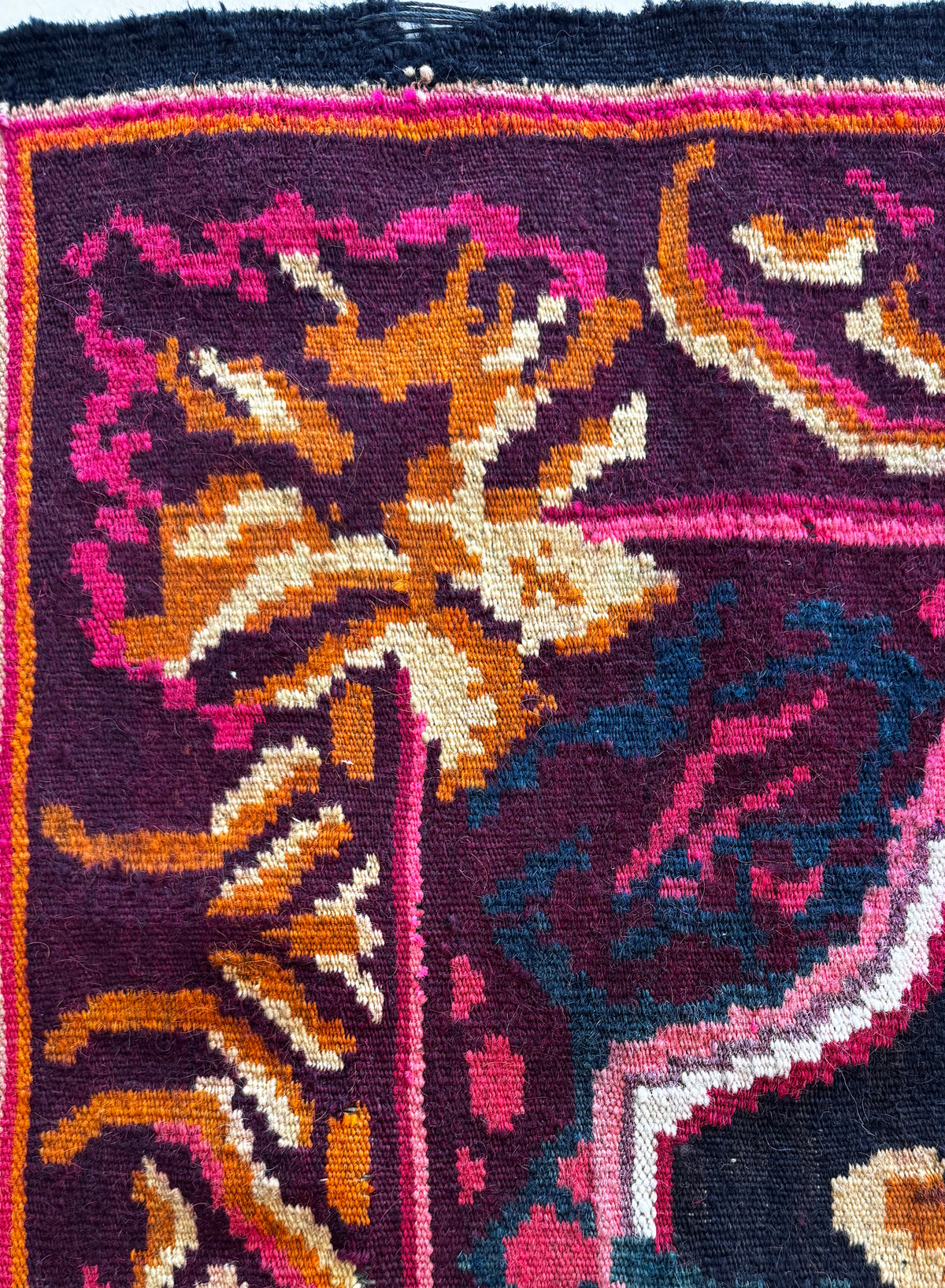 Close-up of a colorful woven rug with a dark navy base and ornate floral and geometric motifs in pink, orange, cream, teal, and purple.