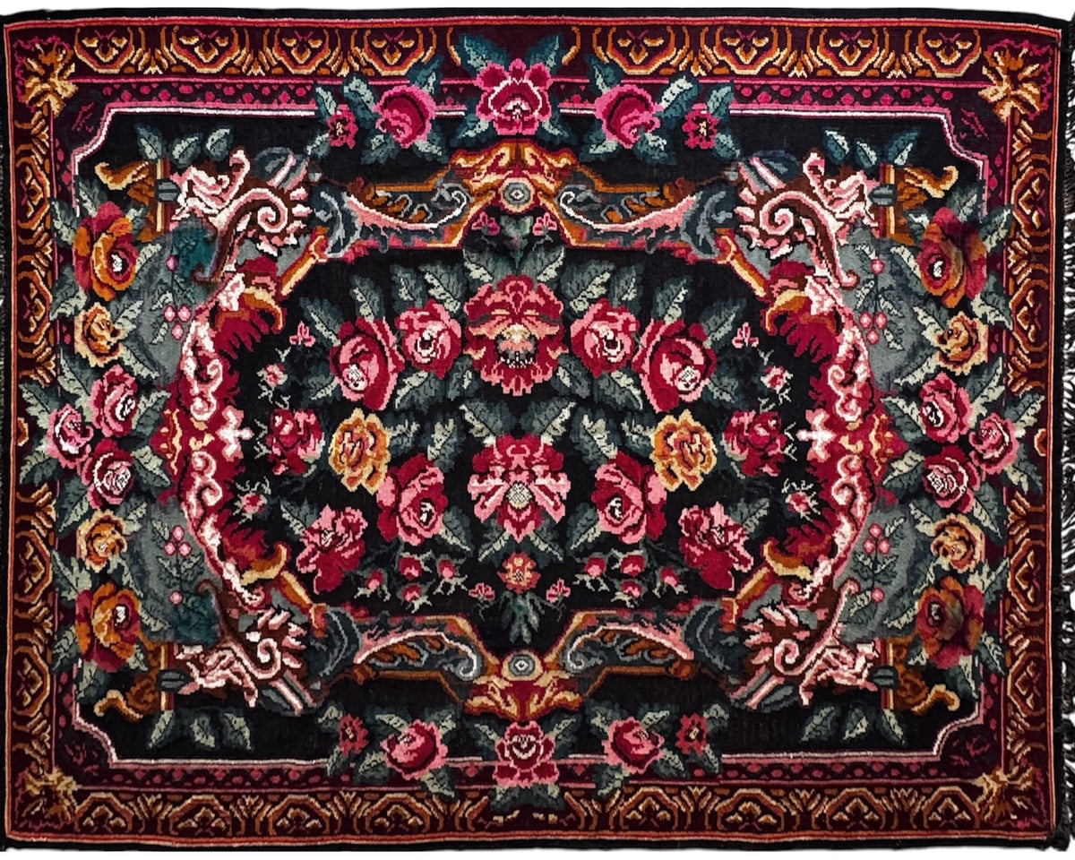 A square area rug with a traditional floral pattern on a black background, featuring red, pink, and gold floral motifs with a dark fringed edge.