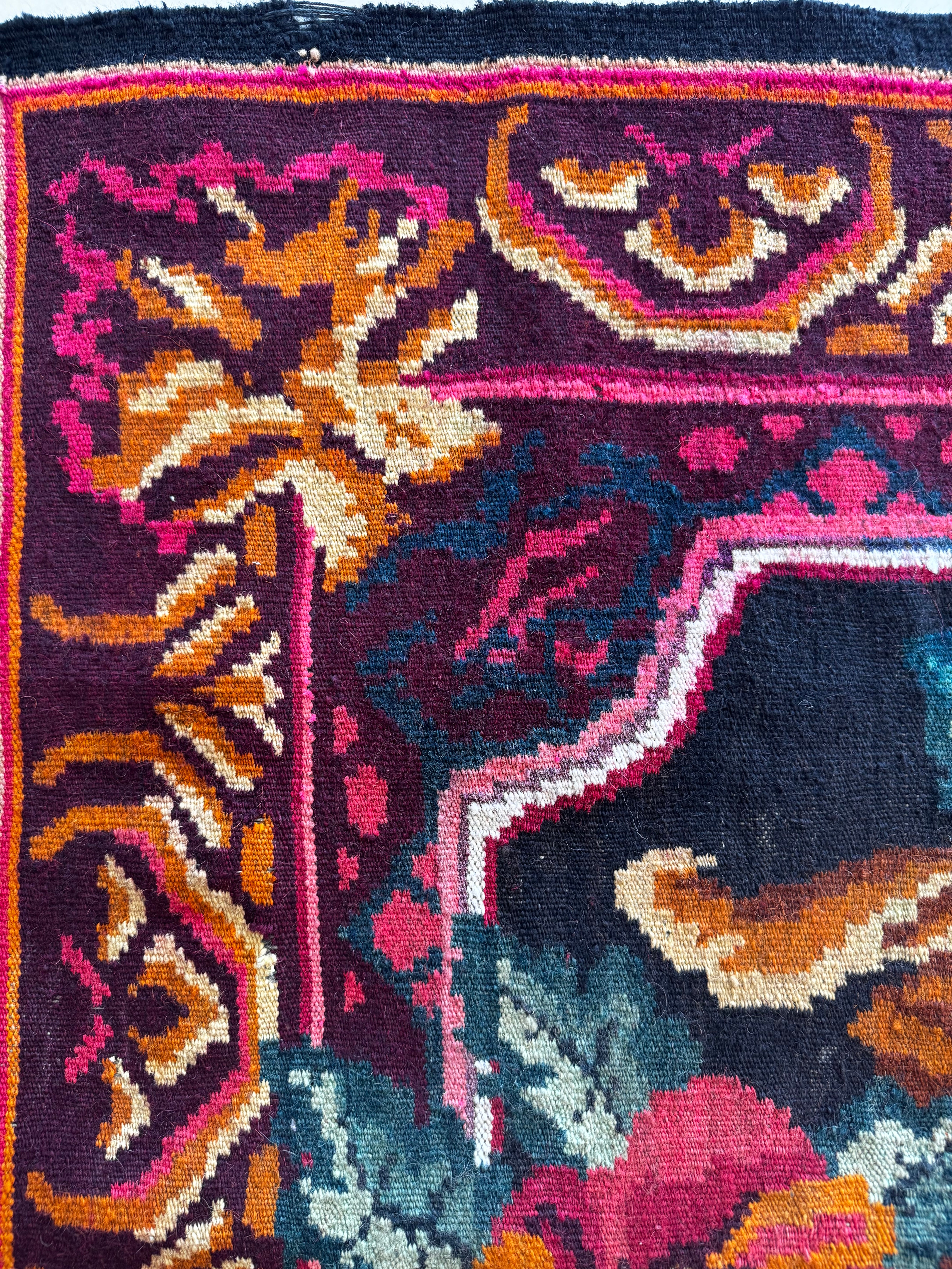 Close-up of a colorful woven rug with a dark navy base and ornate floral and geometric motifs in pink, orange, cream, teal, and purple.