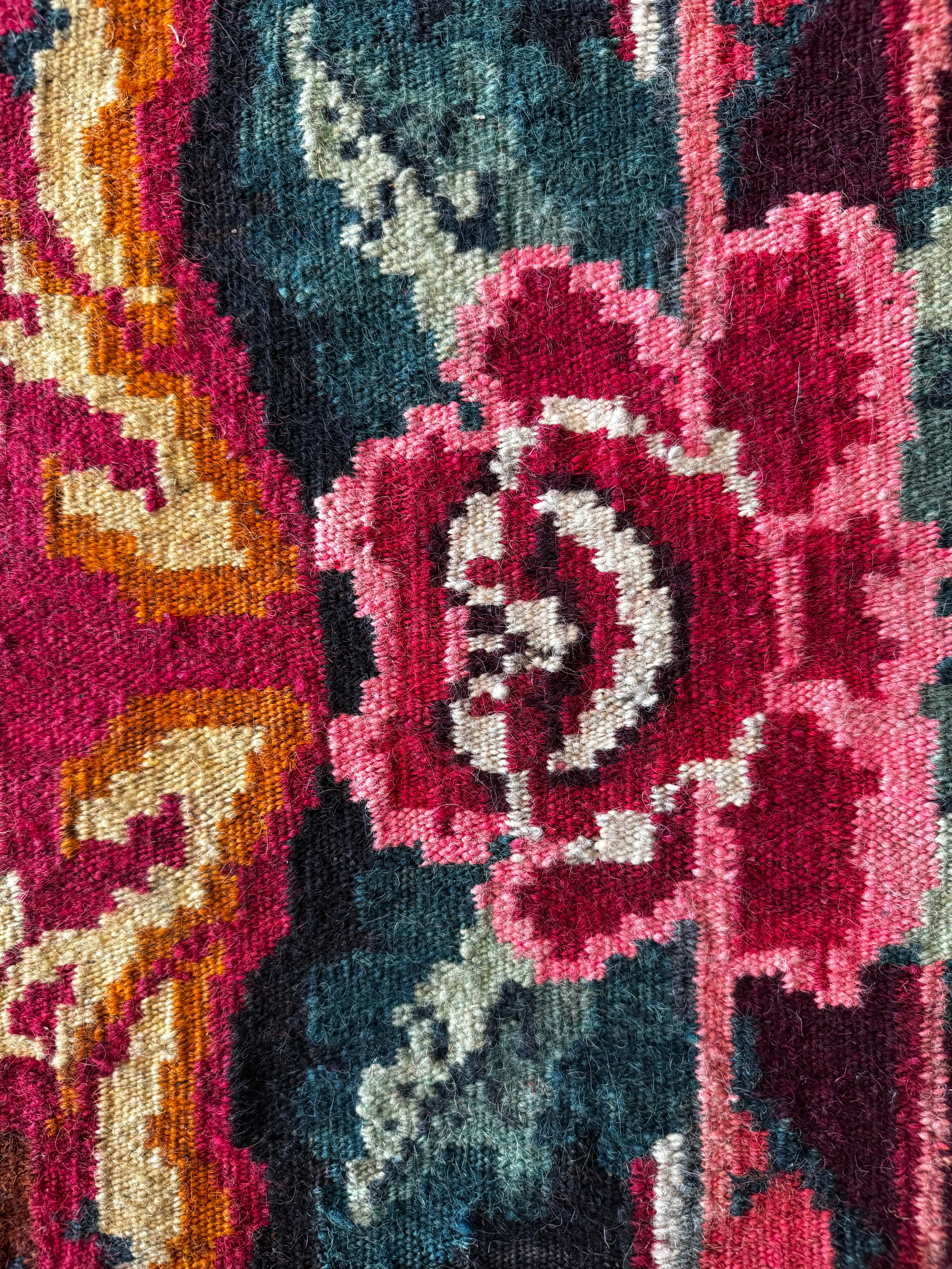 Close-up of a woven textile pattern featuring a large pink and burgundy floral motif with blue-gray, cream, and orange accents.