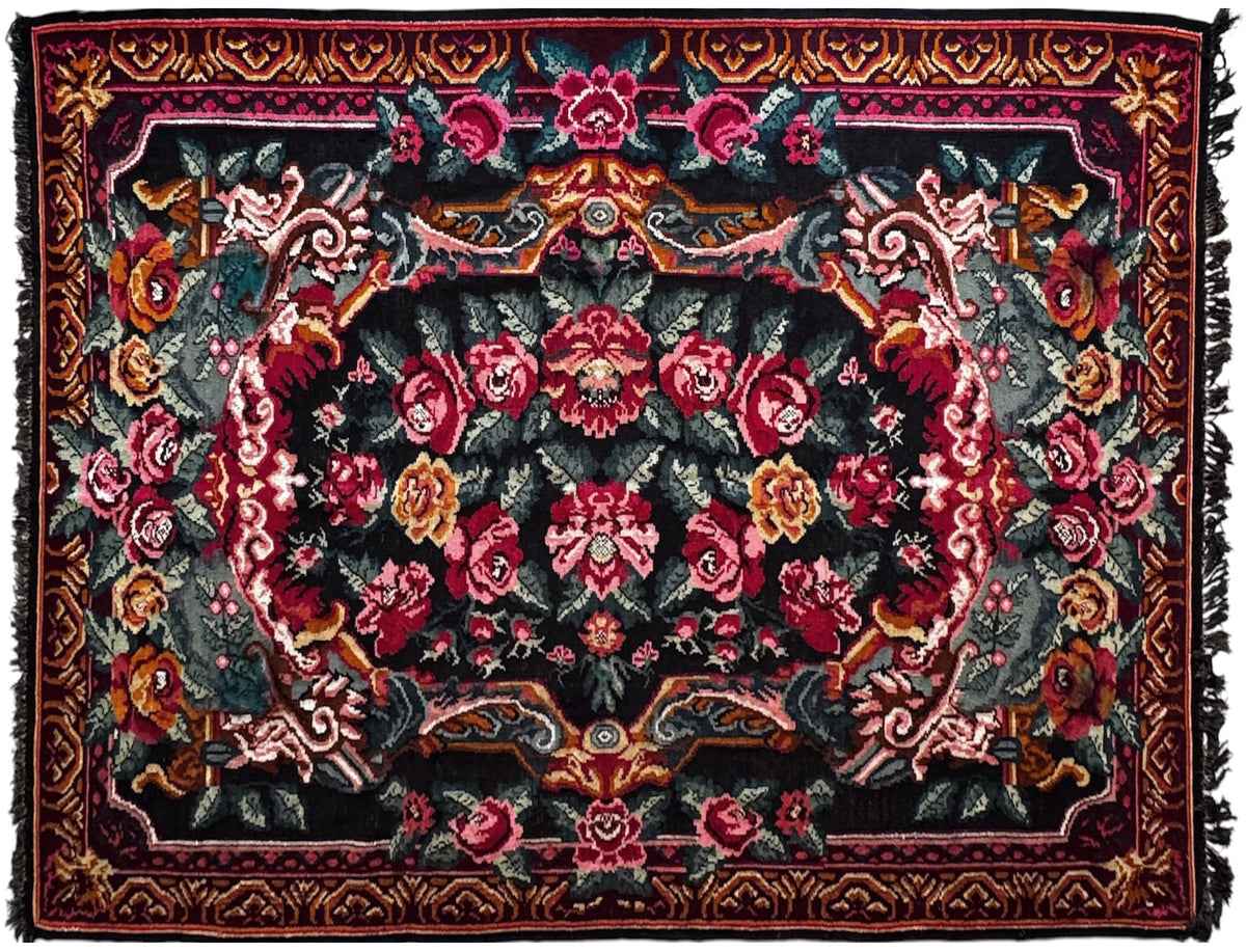 A square area rug with a traditional floral pattern on a black background, featuring red, pink, and gold floral motifs with a dark fringed edge.